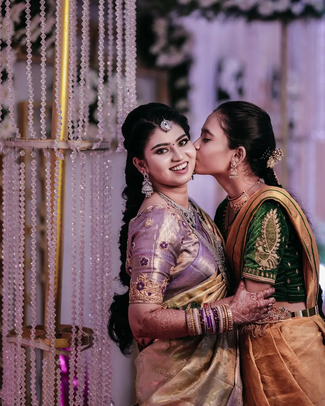 A wedding photographer in Bangalore taking a candid photo of a bride laughing and kissing with her sister