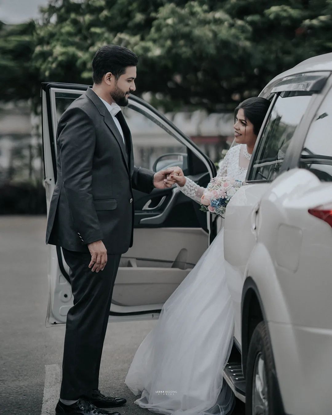 A couple sitting on a car and holding hands at a pre wedding photo shoot in Bangalore, with a garden in the background